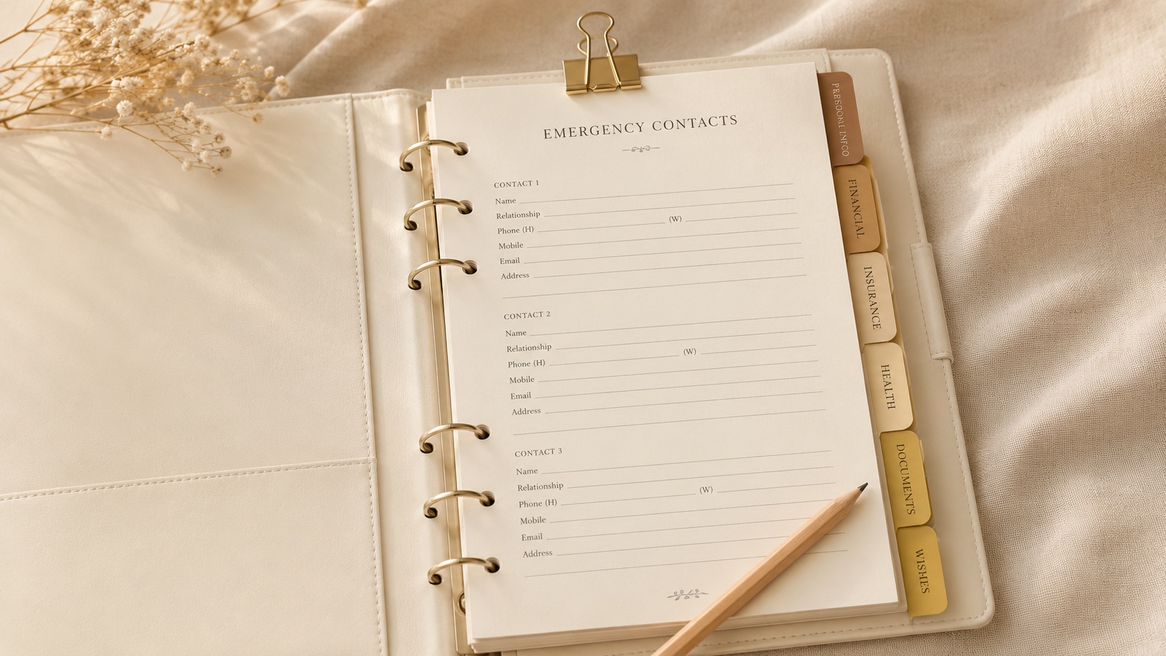 An open family emergency binder showing an Emergency Contacts page with tabbed dividers and a pencil on linen